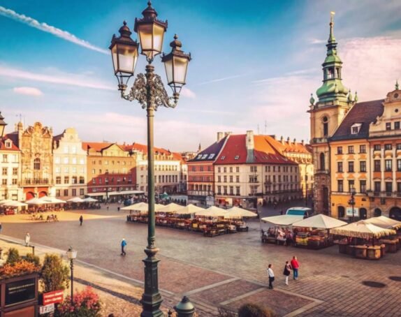 Sunny day in a European city square with historic buildings, street lights and cobblestones.